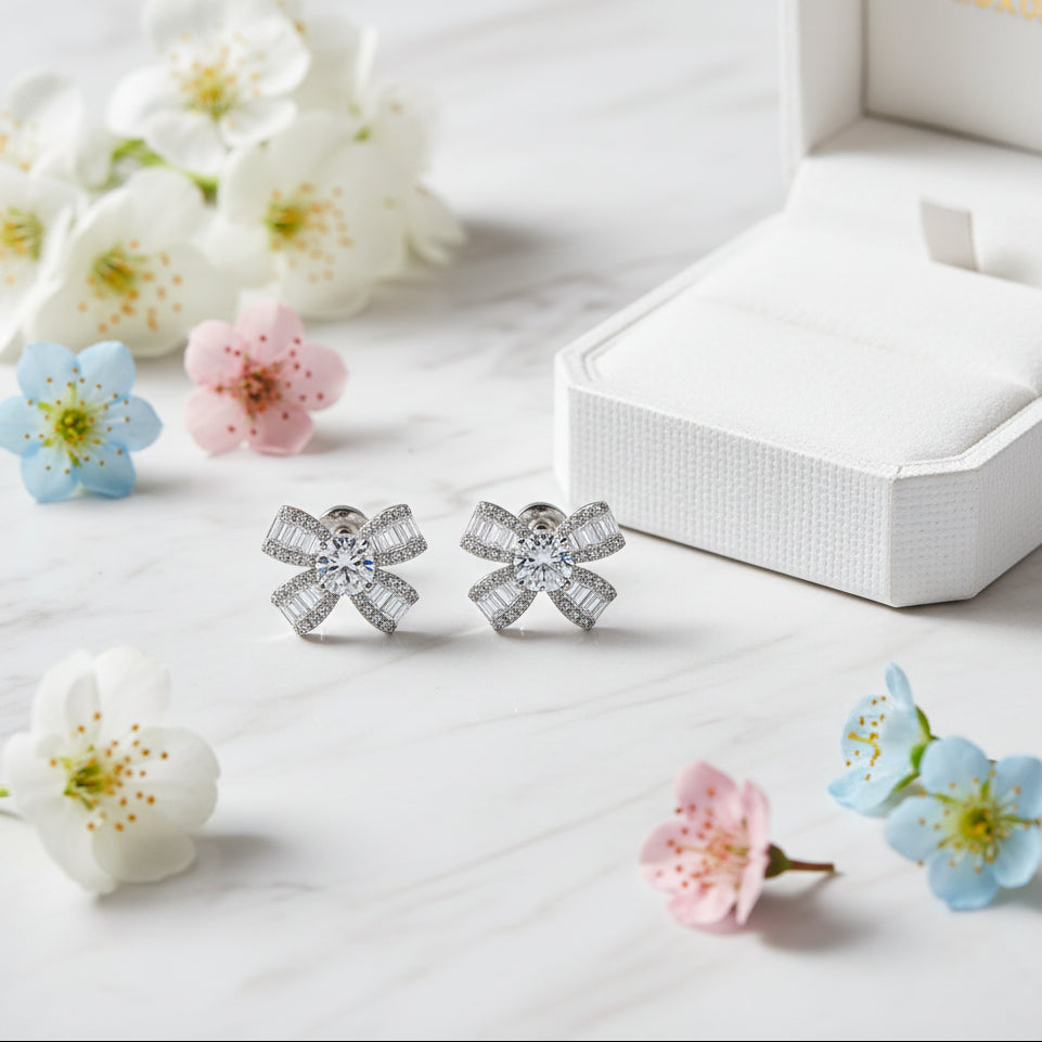 French Bow Design 1 Carat Moissanite Earrings set in Platinum Plated 925 Sterling Silver Capella Reya next to box